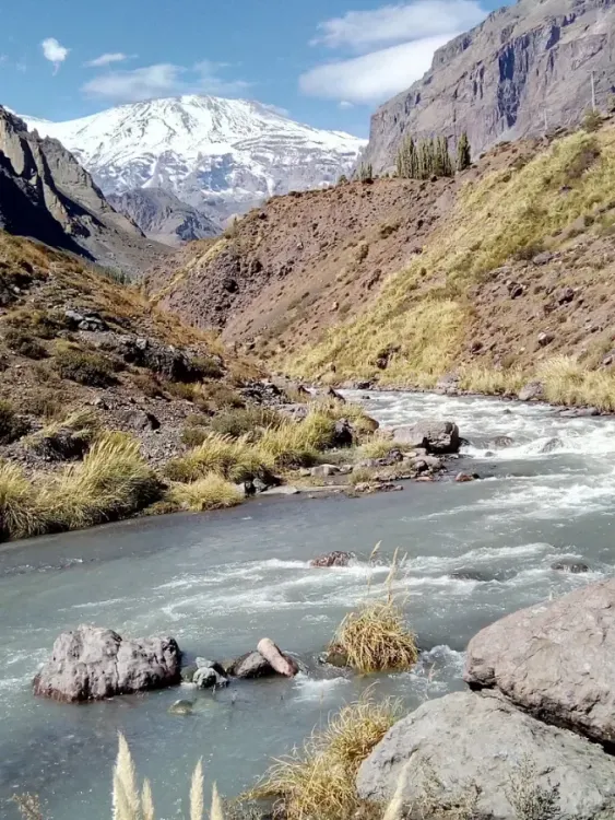 Río de montaña entre laderas rocosas y cumbres nevadas